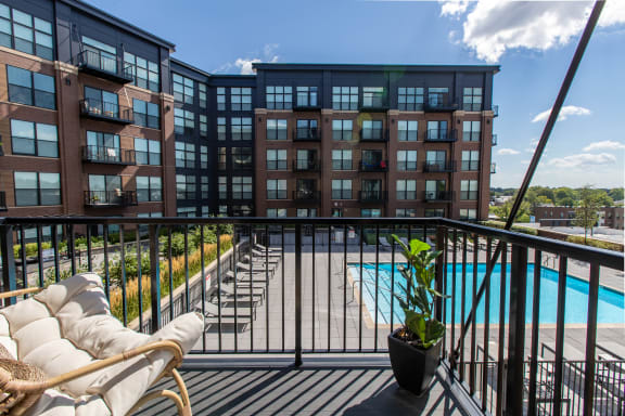 a balcony with a couch and a potted plant and a pool in the background